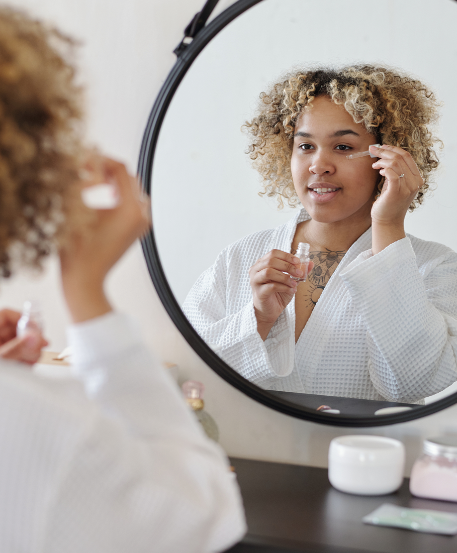 Woman applying skincare product in front of a round mirror