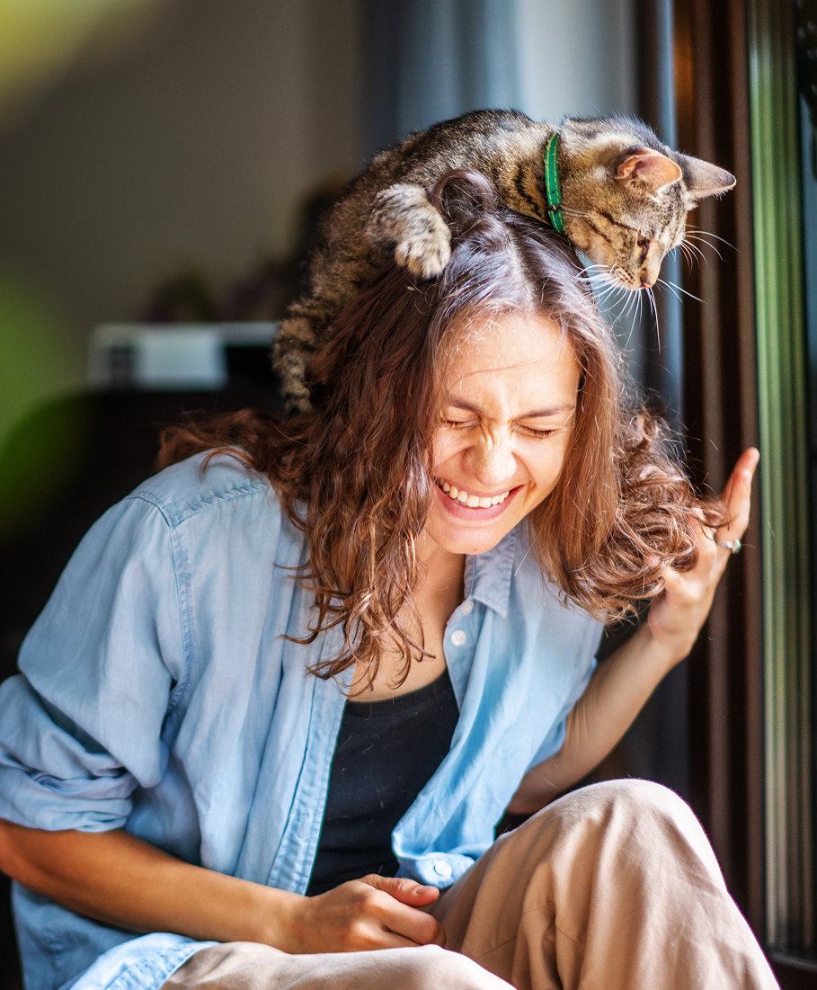 Woman playing with a cat on her head sitting indoors