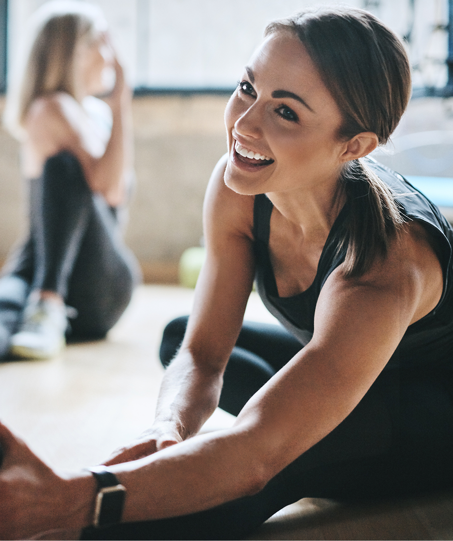 Woman in athletic wear smiling and sitting on a yoga mat in a gym setting