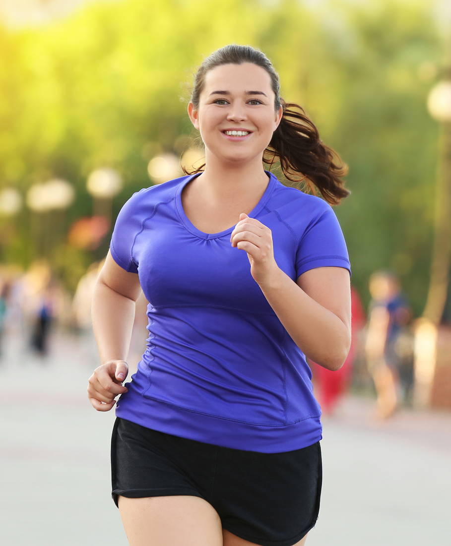 Woman in a blue shirt and black shorts running outdoors with a blurred background