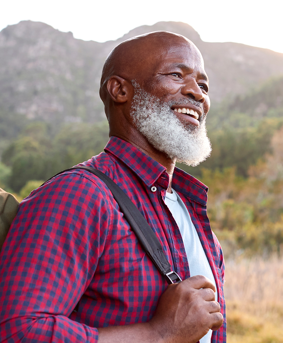 Man with a backpack smiling outdoors with mountains in the background