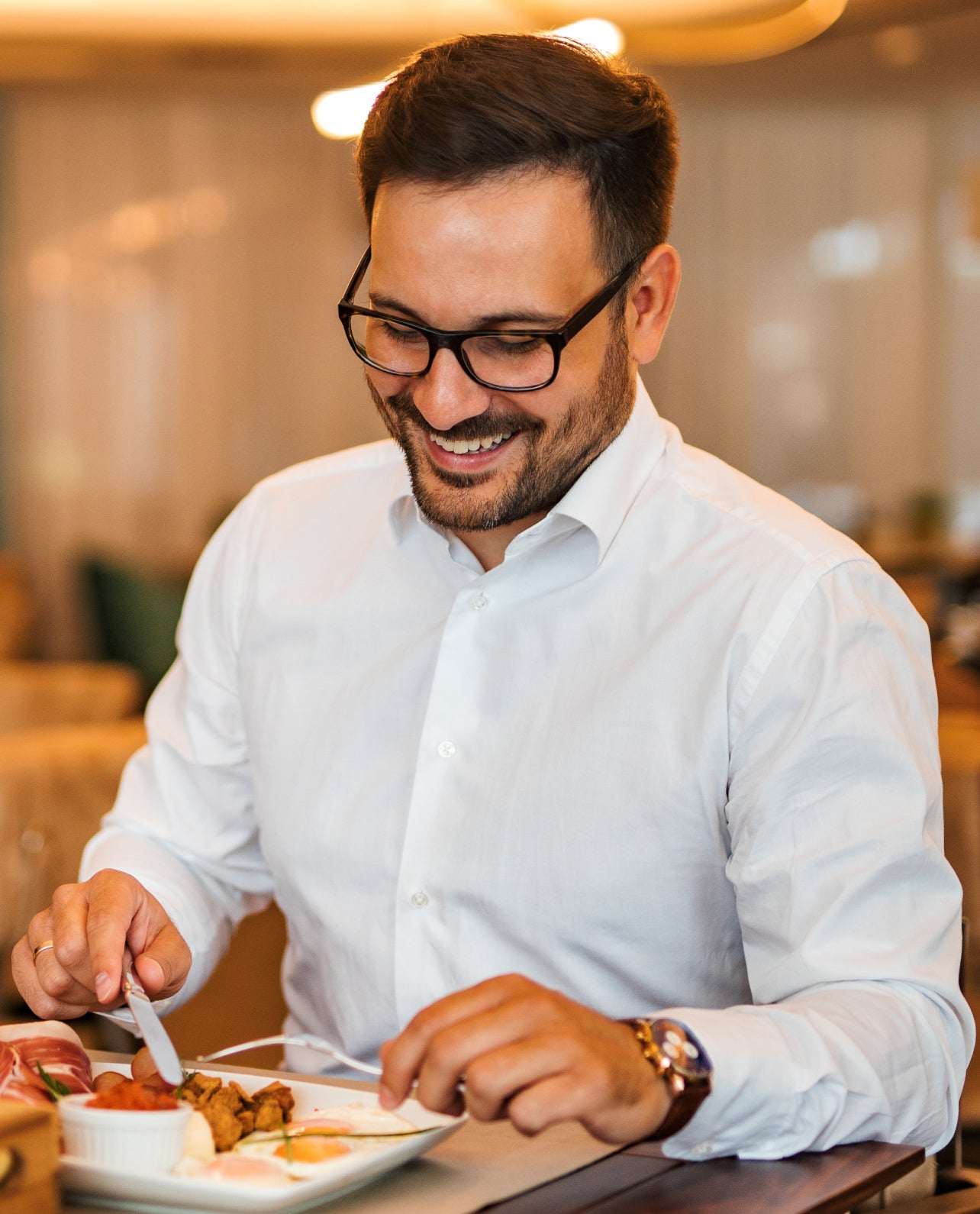 Man in a white shirt and glasses eating at a restaurant table.