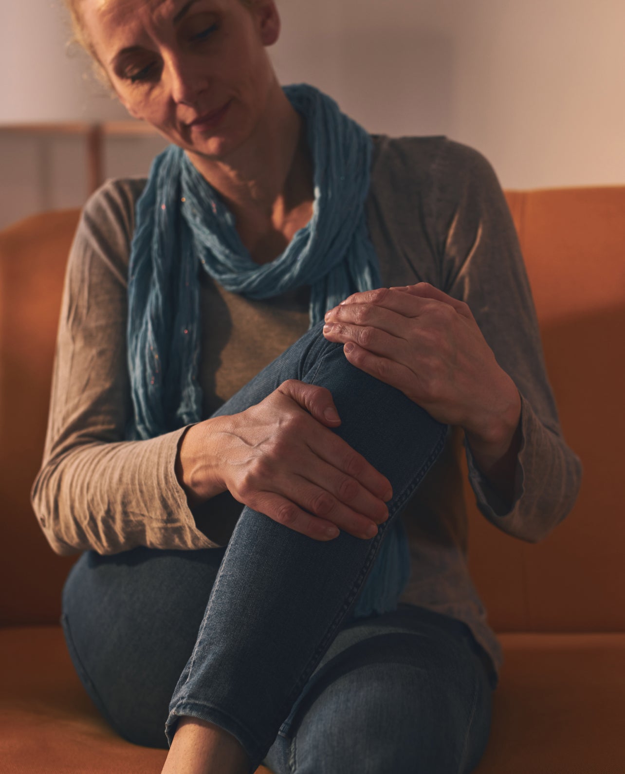 Woman sitting on an orange couch stretching her lower leg muscles.