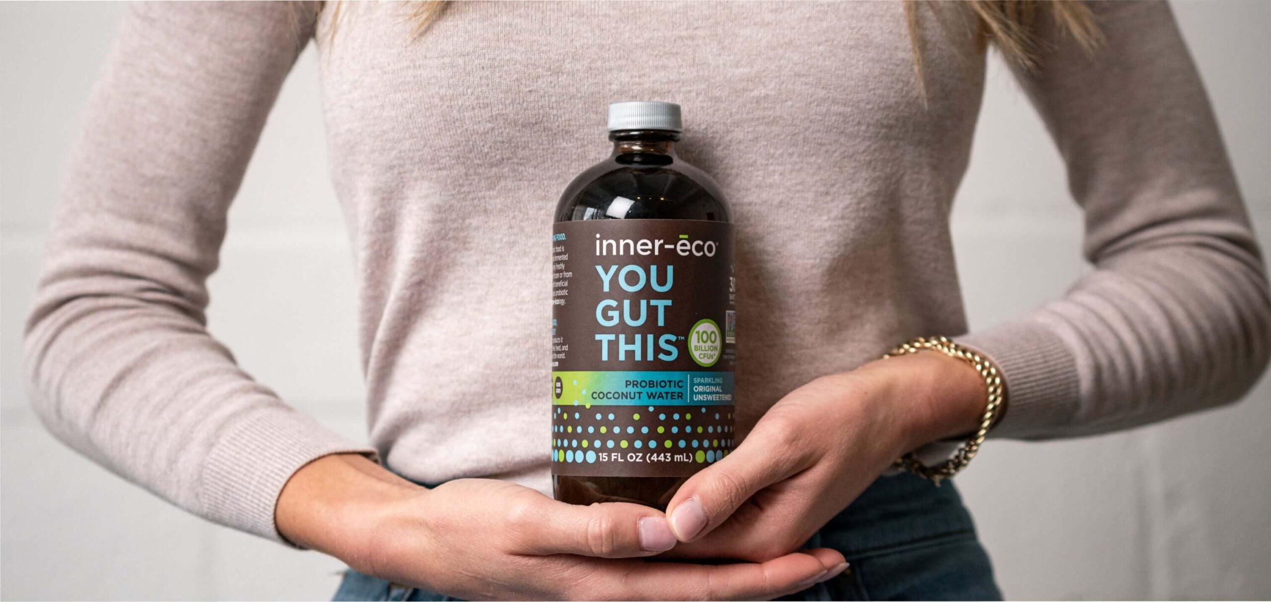 Person holding a bottle of 'inner-eco YOU GUT THIS' supplement against a neutral background