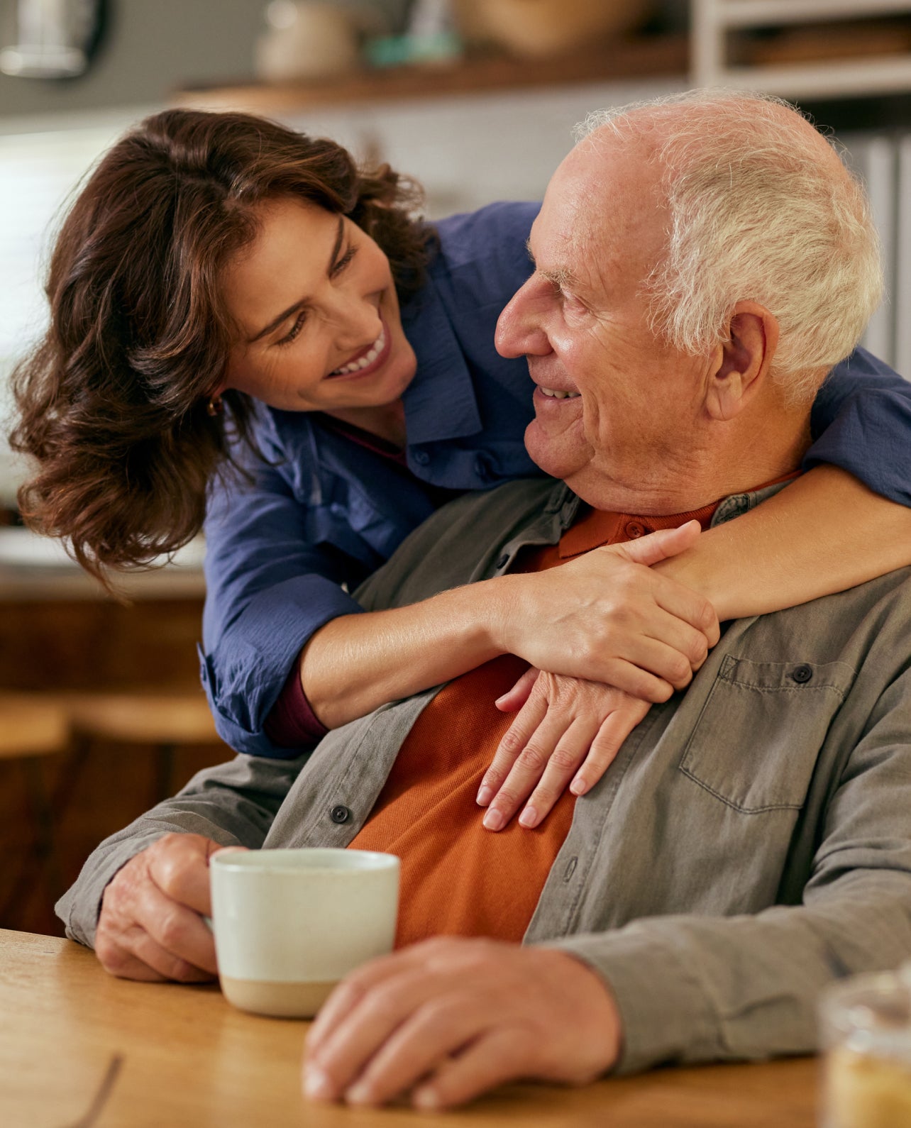 Woman embracing an older man at a table with a cup in the foreground