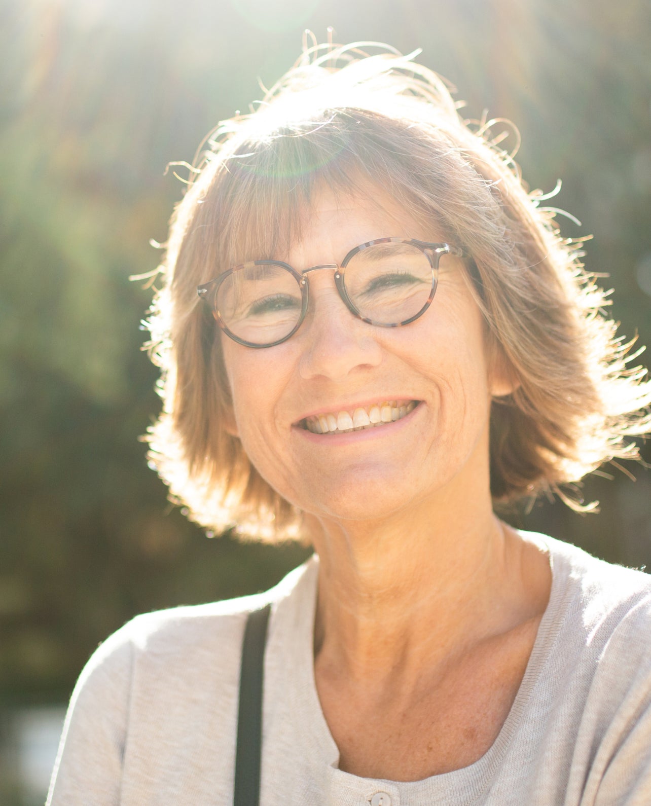 Woman with glasses smiling outdoors with a blurred natural background