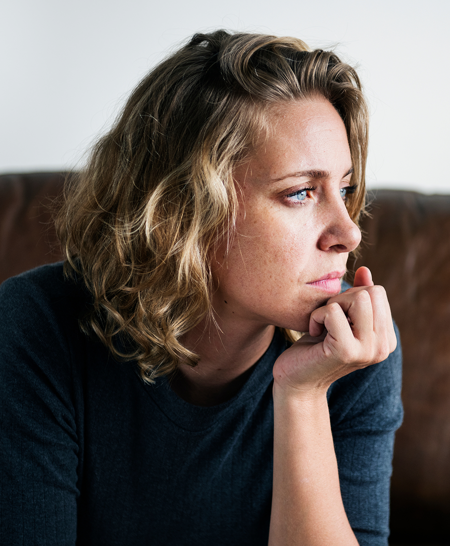 Woman with blonde hair and blue eyes sitting on a couch, looking thoughtful.