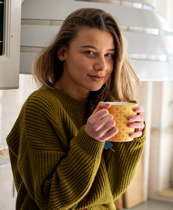 Woman holding a yellow mug with a pattern, wearing a green sweater indoors.
