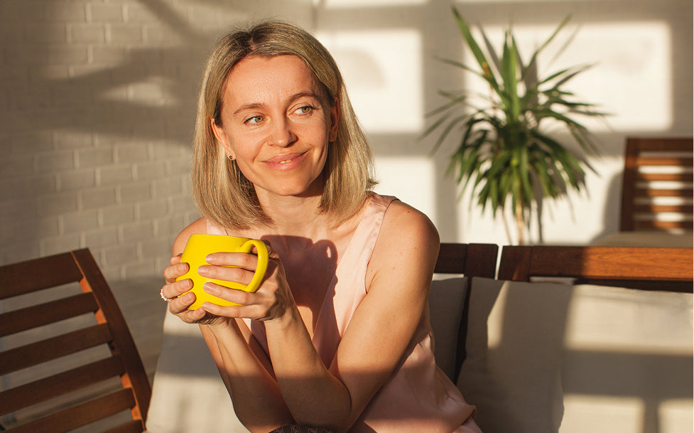 Woman holding a yellow mug in a sunlit room with a plant in the background