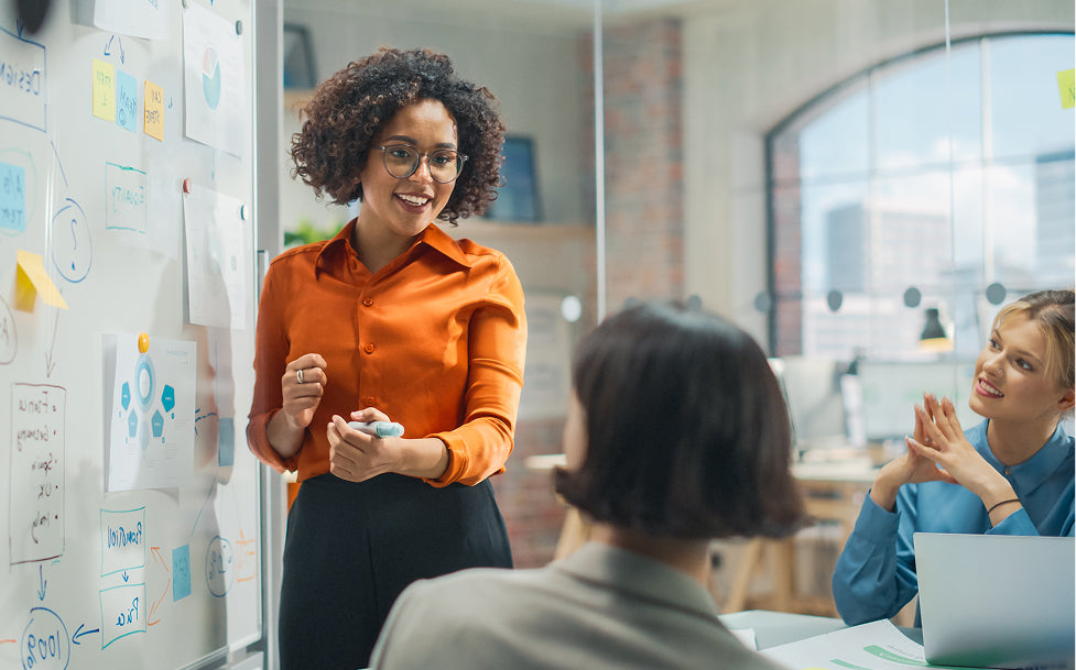 Woman in orange shirt presenting to colleagues in a modern office setting