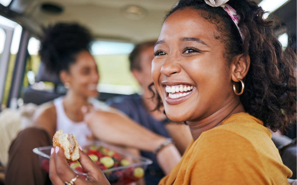Woman smiling and eating a sandwich in a car with friends