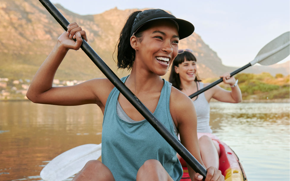 Two women paddling in a kayak on a lake with mountains in the background