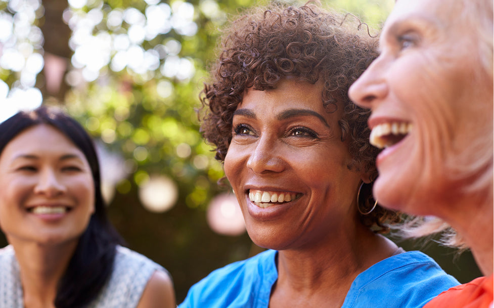 Three women smiling outdoors with a blurred natural background