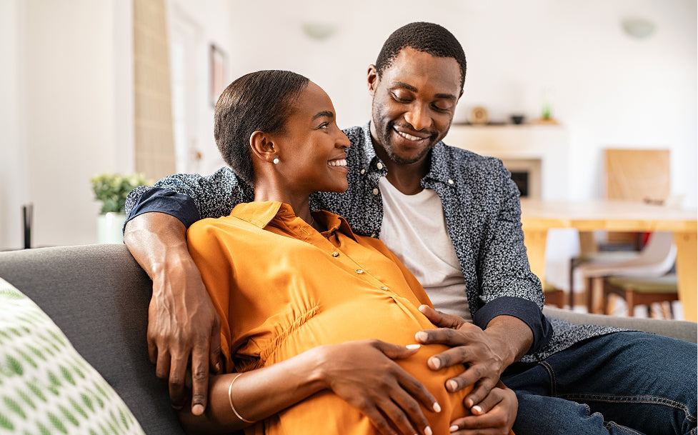 Pregnant woman sitting on a couch with a man, both smiling.