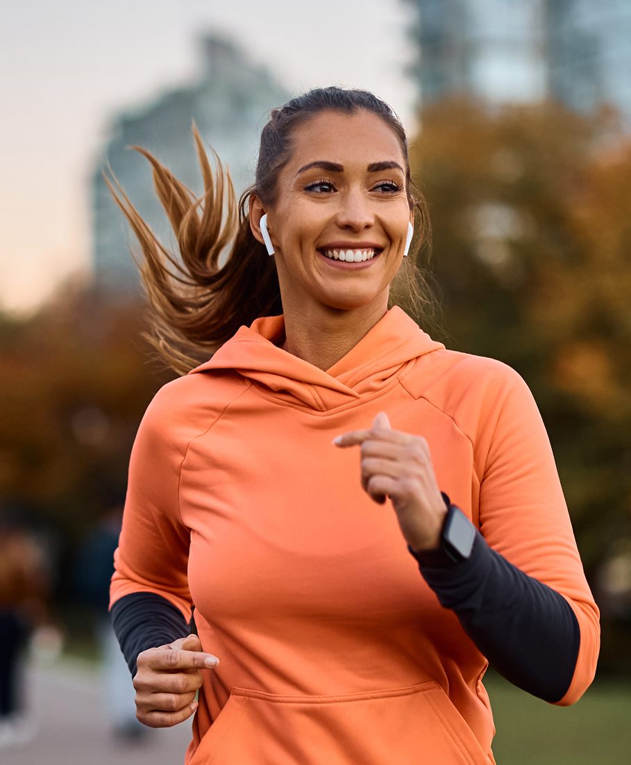 Woman in an orange hoodie running outdoors with a blurred background