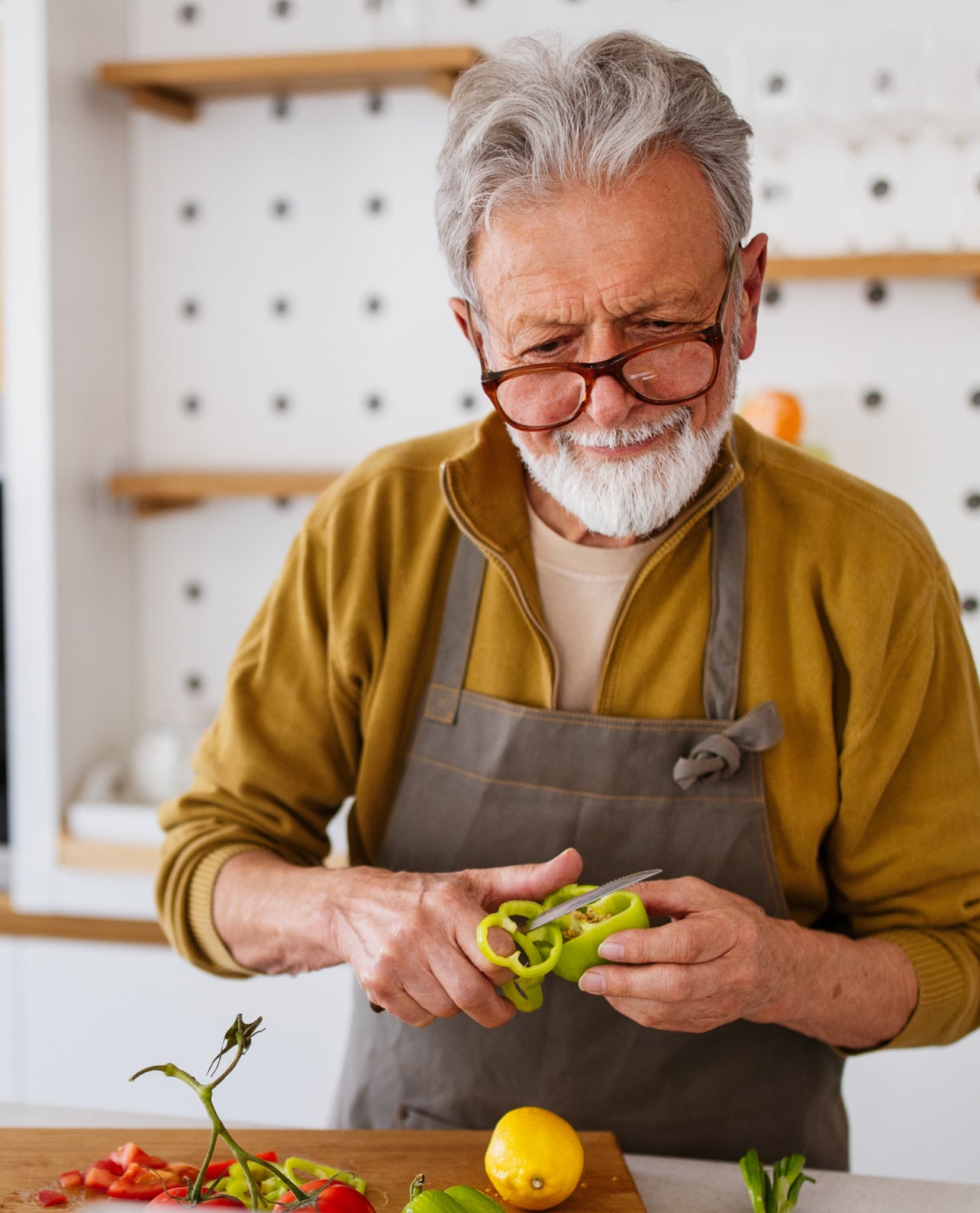 Man in a kitchen cutting a green pepper over a wooden cutting board.