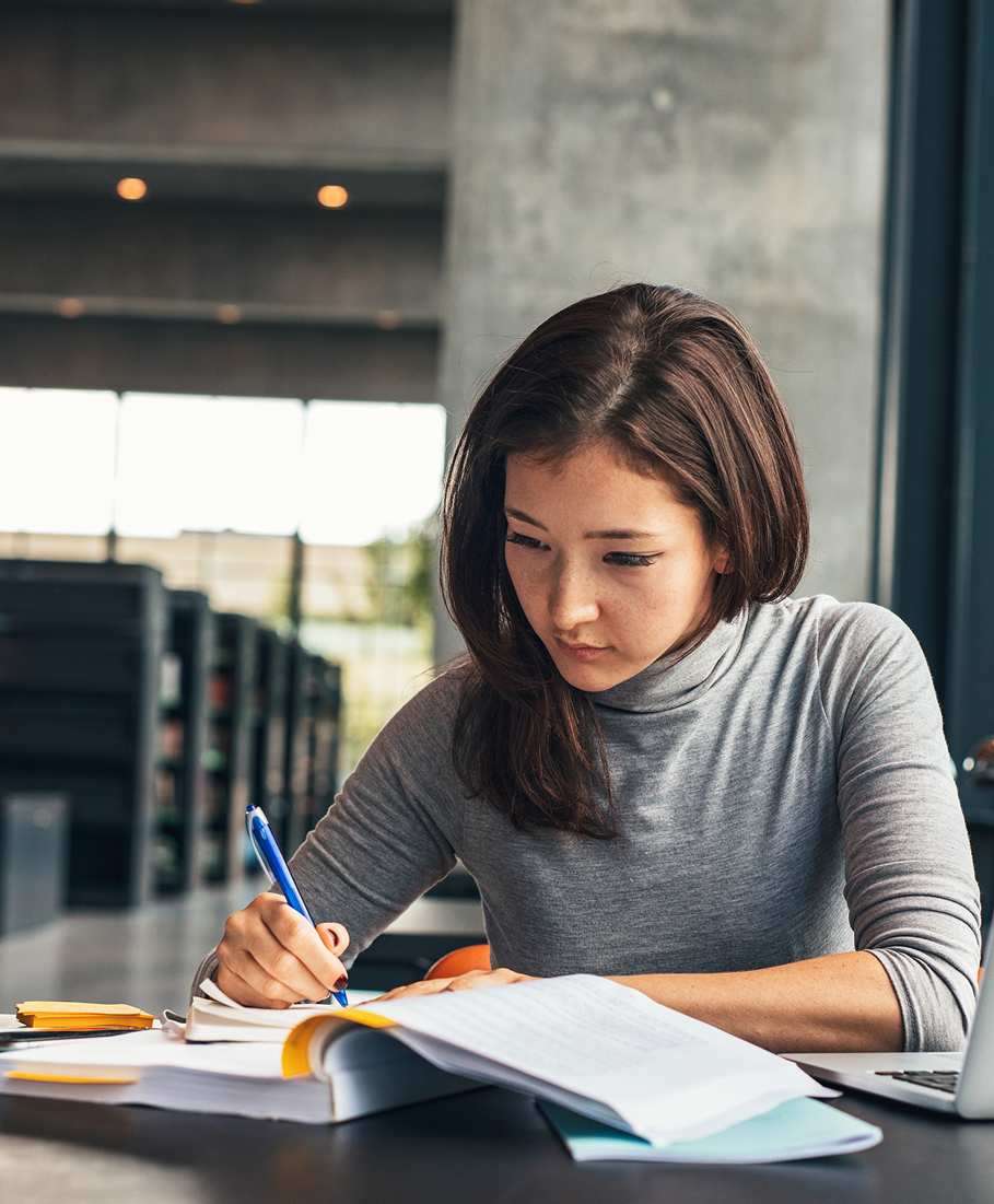 Woman studying with books and a pen in a library setting