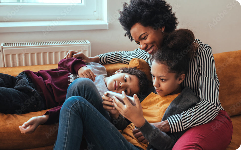 Woman and two children sitting on a couch, looking at a tablet together.