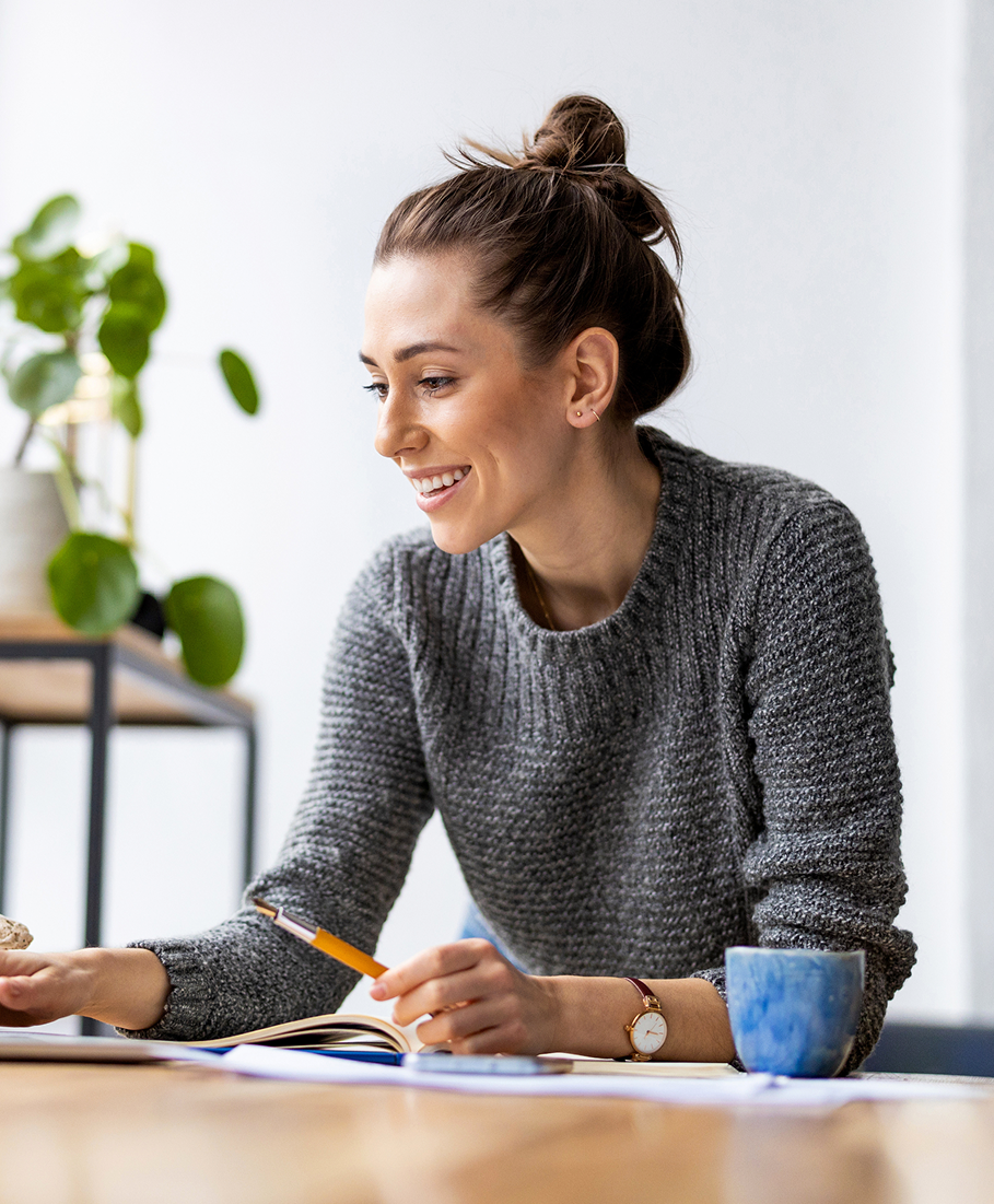 Woman sitting at a table with a notebook and pencil, smiling.