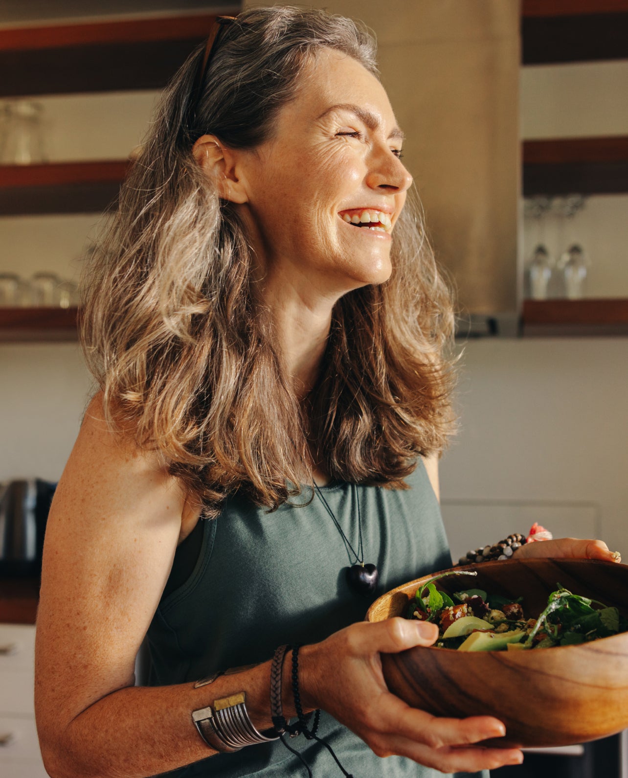 Woman holding a wooden bowl of salad in a kitchen setting