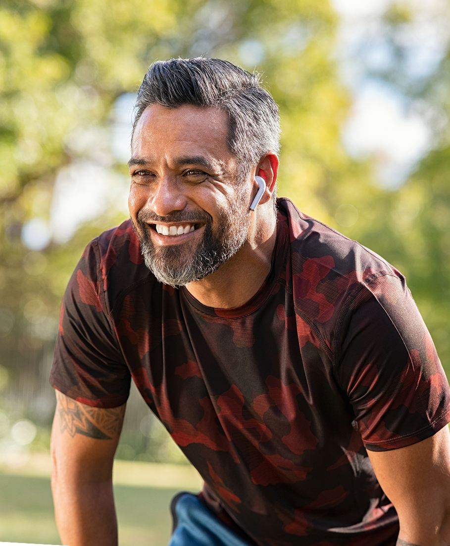 Man wearing a red and black patterned shirt pausing during a run outdoors with greenery in the background
