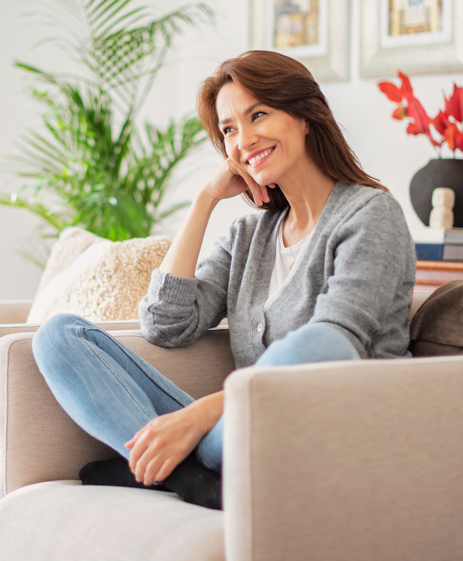 Woman sitting on a couch in a living room with plants and decor.
