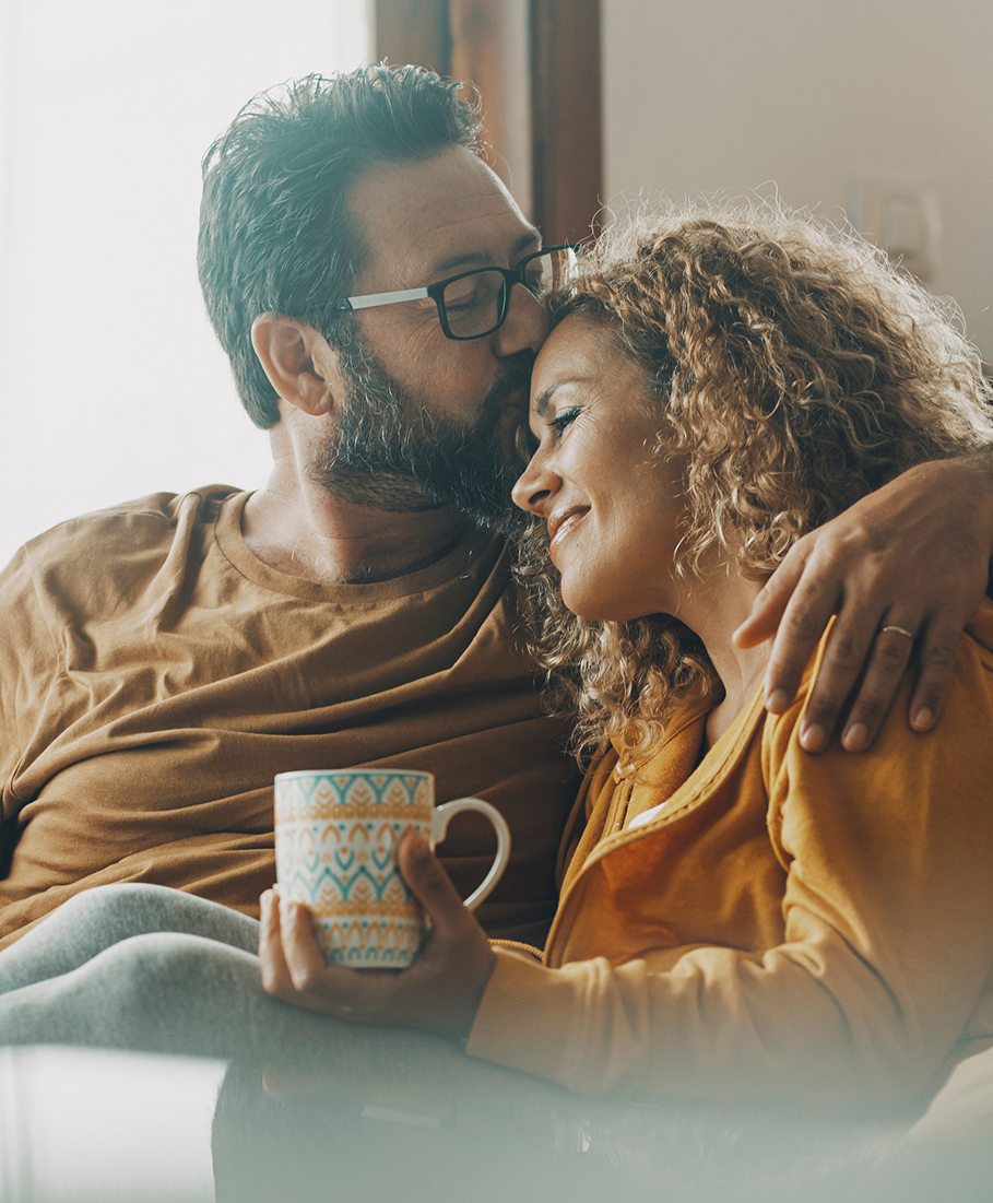 Man and woman embracing with a mug, sitting together indoors.