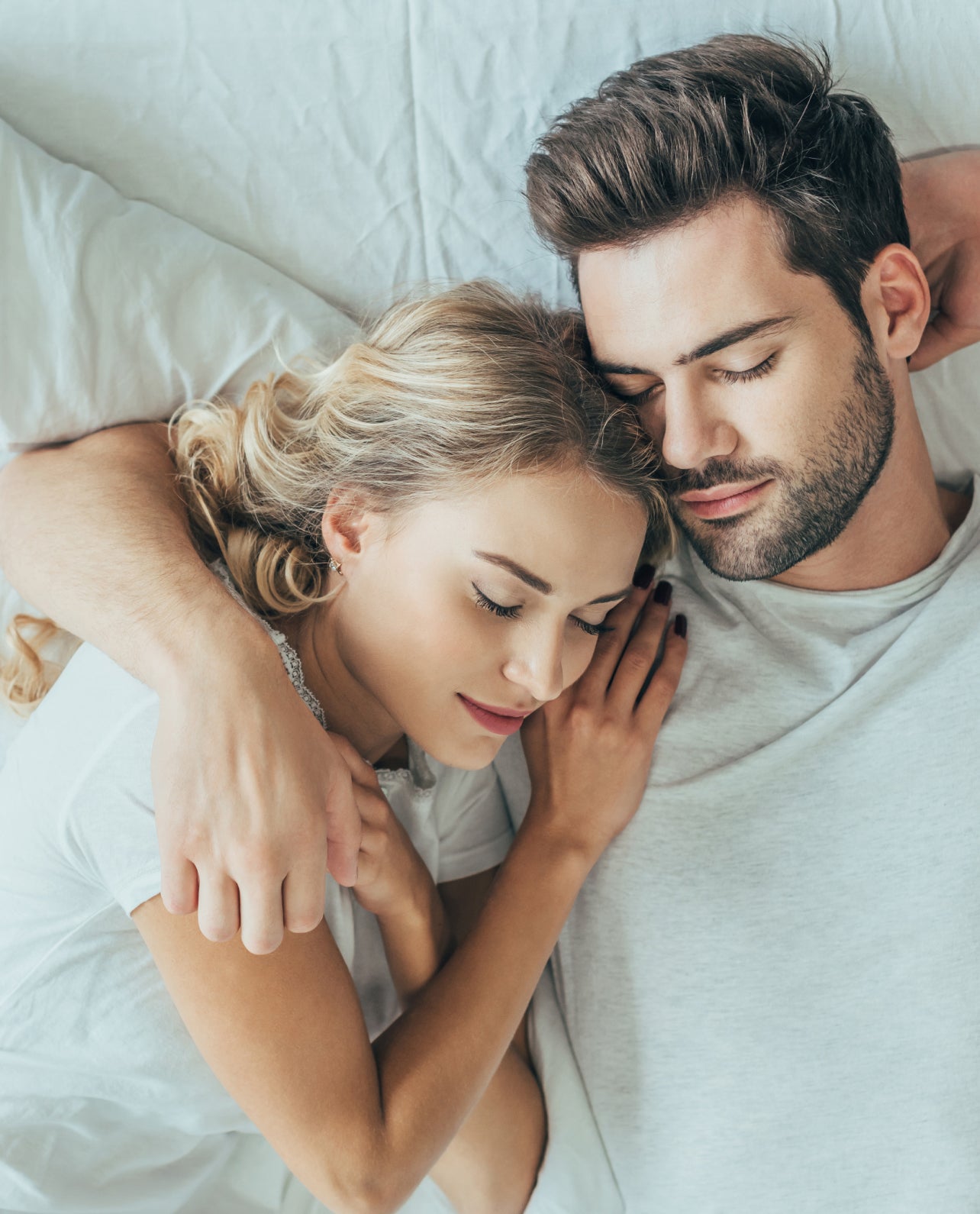 Man and woman embracing in bed, with the woman resting on the man's shoulder.
