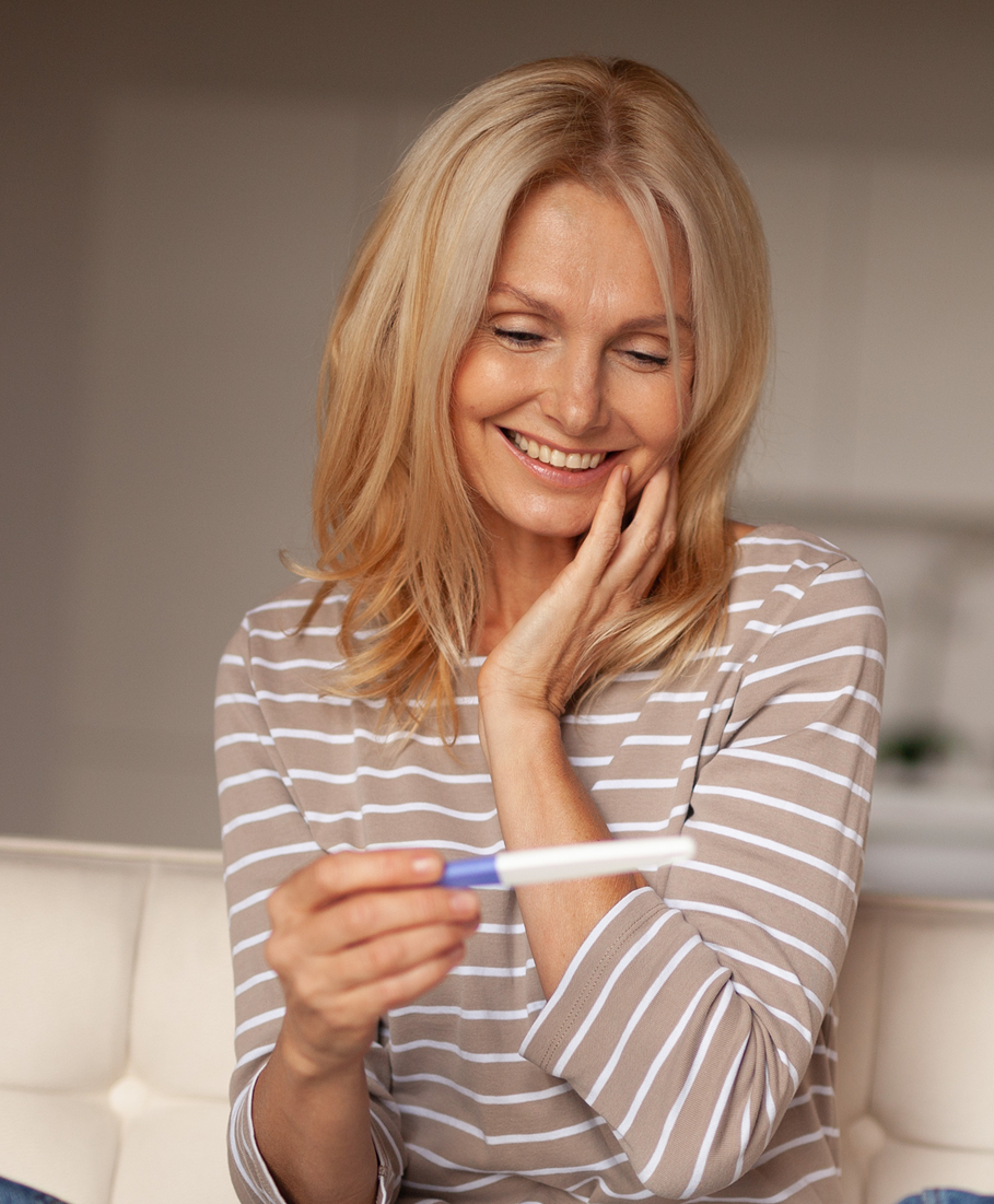 Woman holding a pregnancy test with a happy expression indoors.