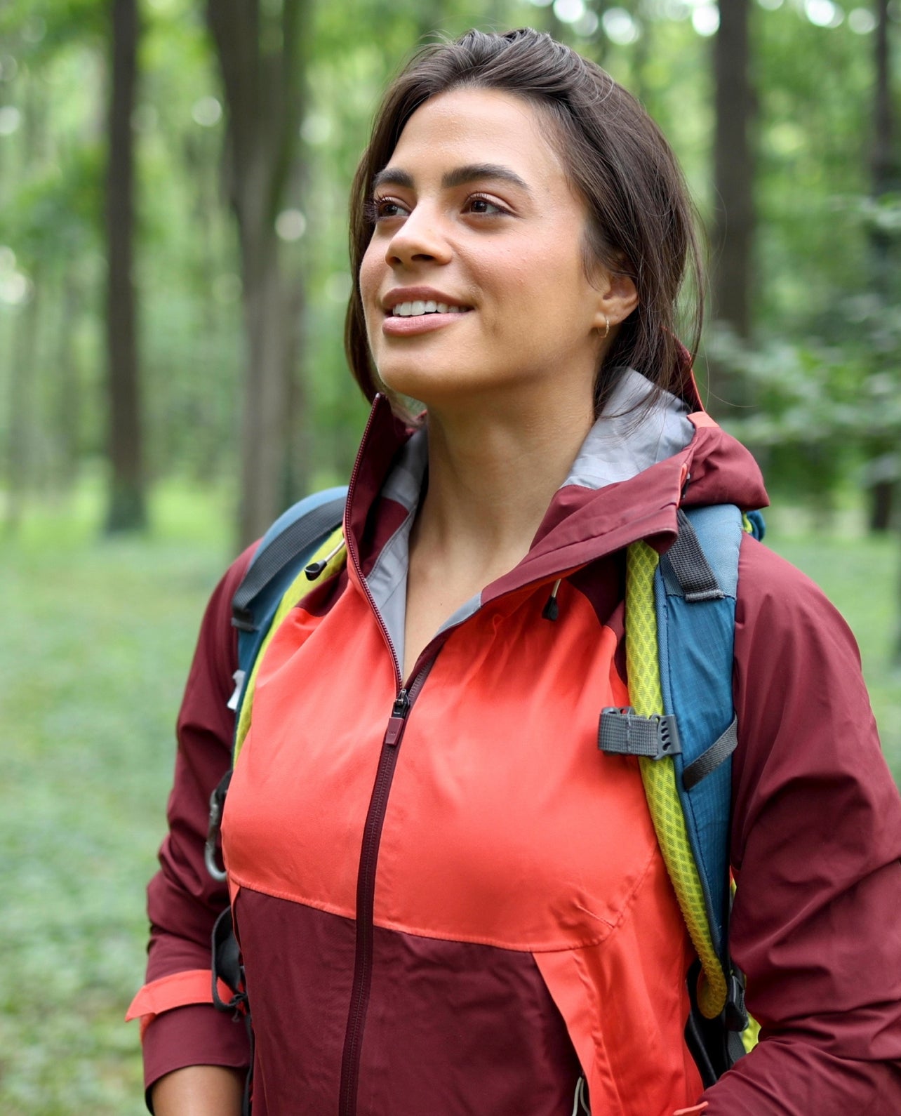 Woman hiking in a forest wearing a red and maroon jacket with a backpack.