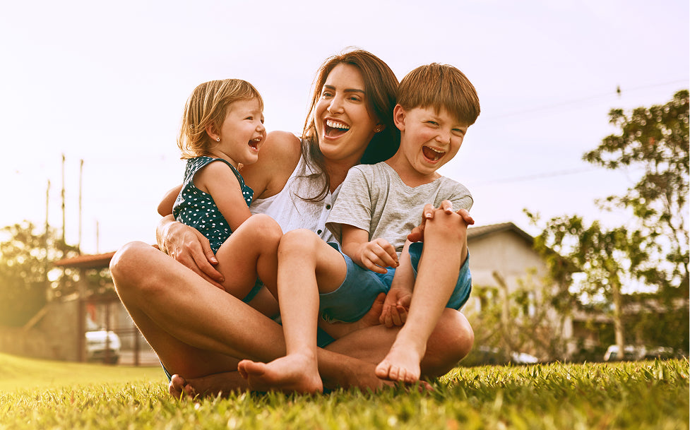 Woman sitting on grass with two children, all smiling outdoors