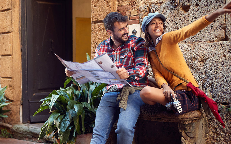 Two people sitting on a stone bench looking at a map outside a building.