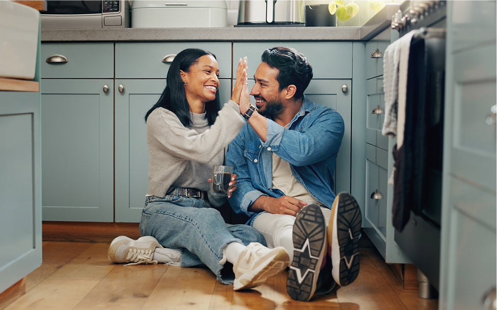 Man and woman sitting on a kitchen floor, high-fiving, with a casual and happy atmosphere.