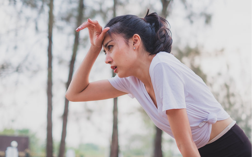Woman catching her breath in athletic wear outdoors with trees in the background