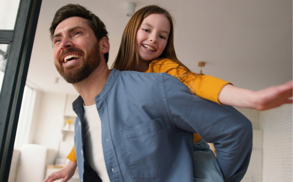 Man and young girl balanced on his back smiling indoors