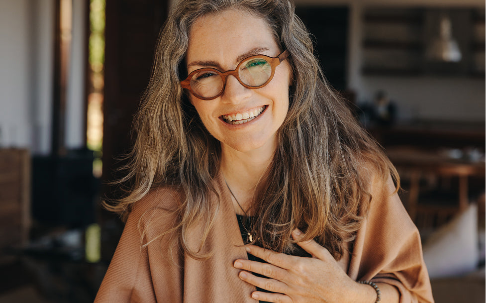 Woman wearing glasses and a brown top, smiling indoors.