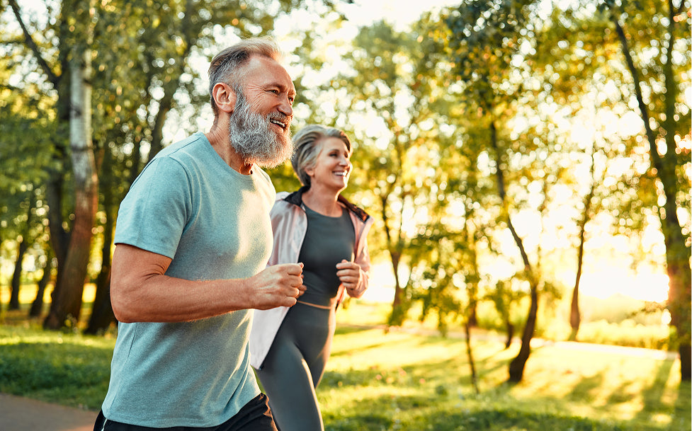Man and woman jogging together in a park with trees and sunlight filtering through.