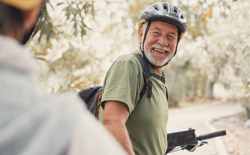 Man with a helmet and backpack standing outdoors on a bike path.