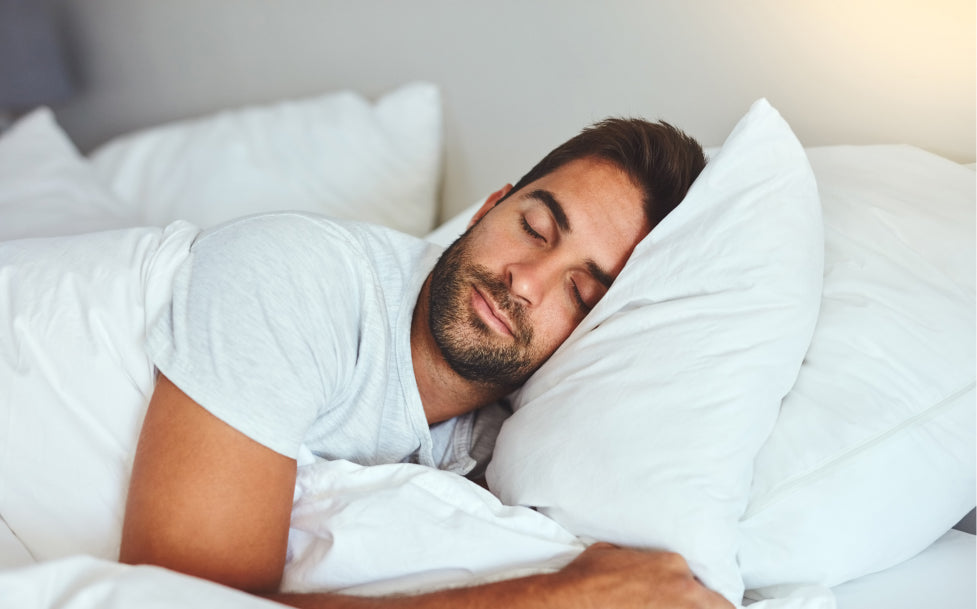 Man sleeping peacefully in bed with white pillows and sheets.