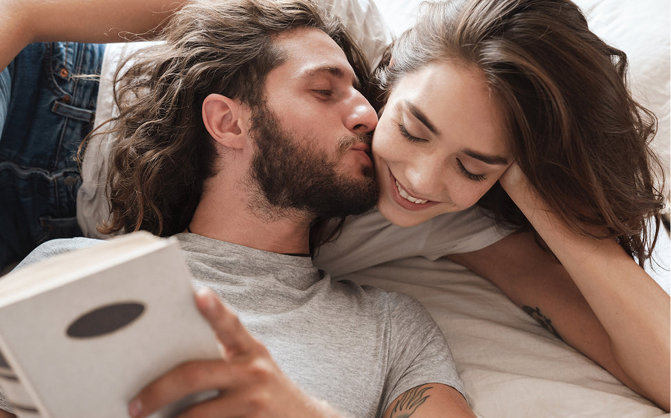 Couple lying on a bed, man reading a book to woman