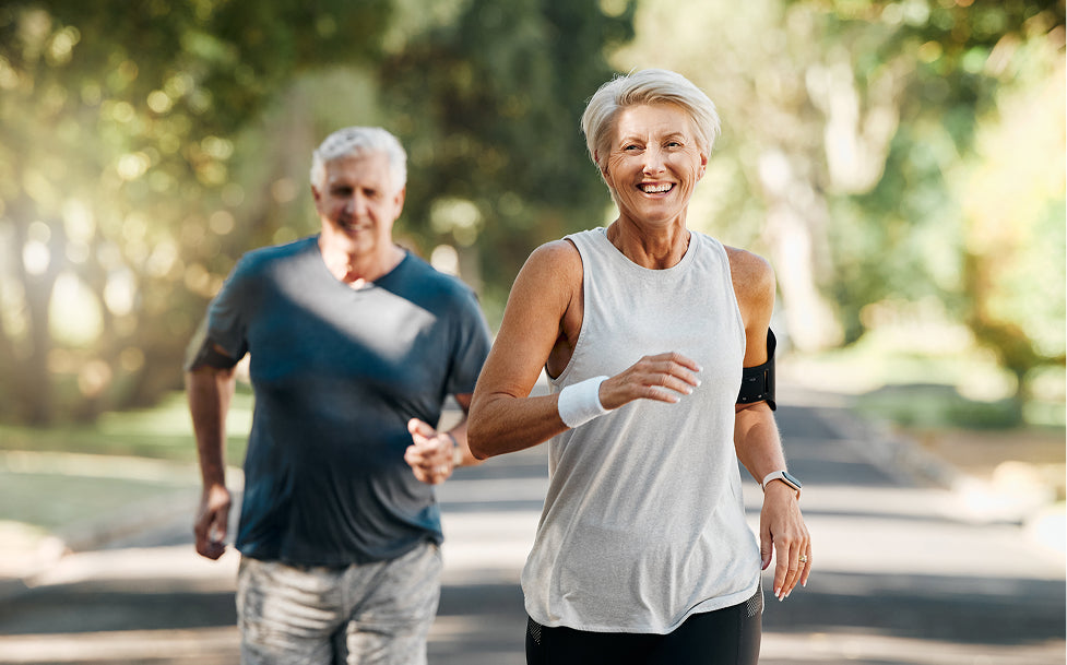 Two elderly people running outdoors on a path with trees in the background